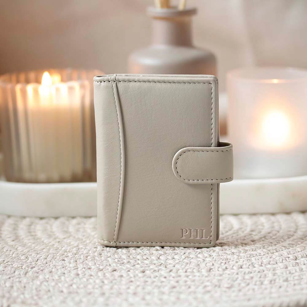 Light gray leather wallet with 'PHIL' monogram on a textured surface with candles in the background