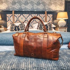 Orion tan leather holdall travel bag by Primehide on bed in travel setting, showing premium finish and design.